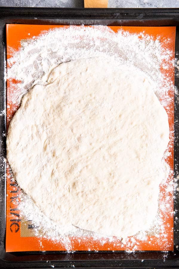 pizza dough rolled out into a circle, on a baking sheet with a silpat mat