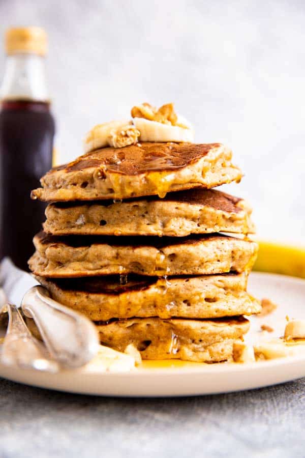 stack of banana pancakes with a bottle of syrup behind it