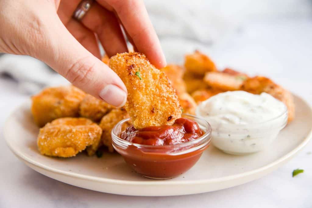 female hand dipping a chicken nugget in a bowl with ketchup