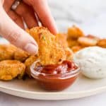 female hand dipping a chicken nugget in a bowl with ketchup