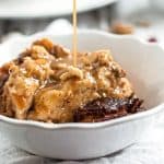 close up photo of a white bowl filled with bread pudding, with fudge sauce drizzling over