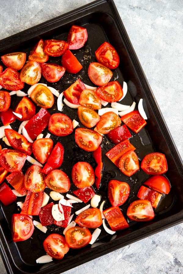 dark baking pan with cut up tomatoes, red pepper, onion and garlic