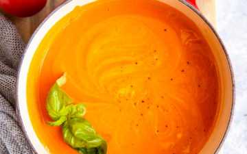 red cast iron pot with homemade tomato soup, surrounded by fresh tomatoes and basil