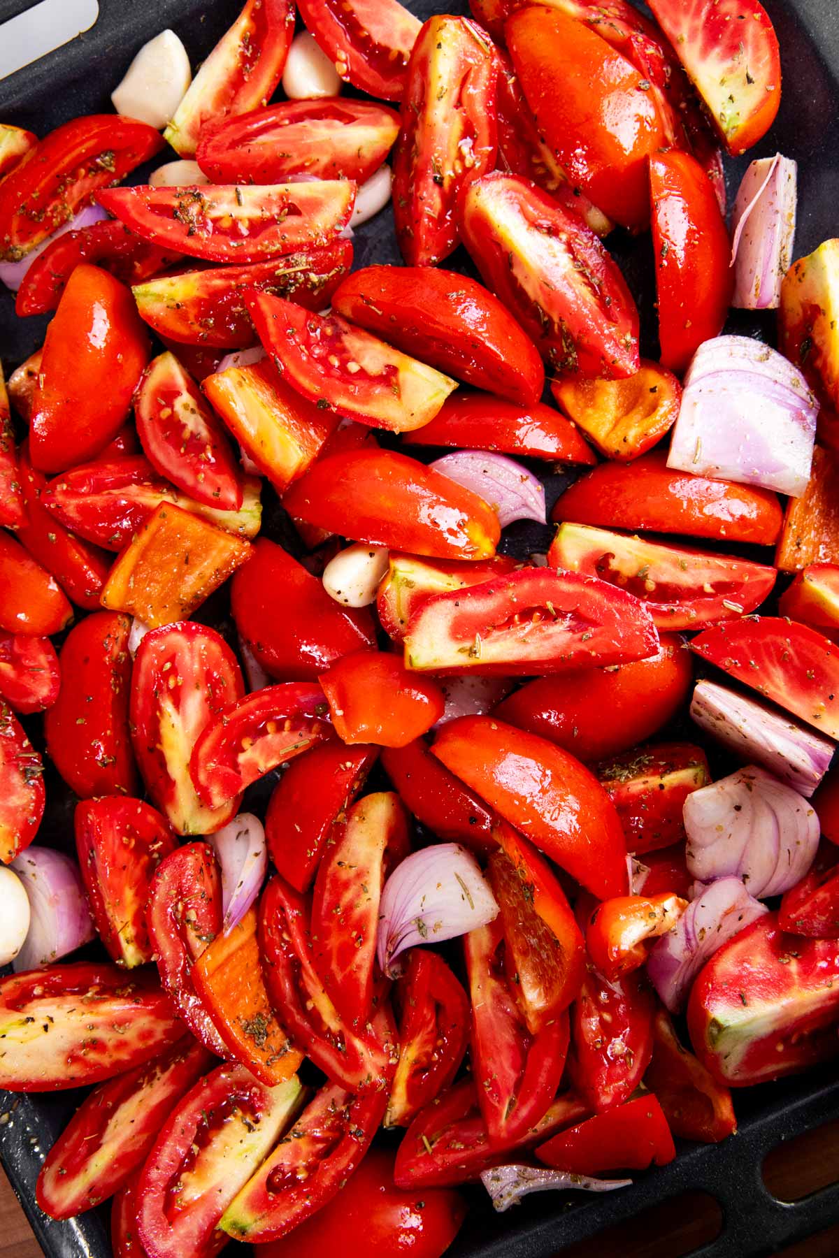 Raw cut up tomatoes and aromatics on a sheet pan.