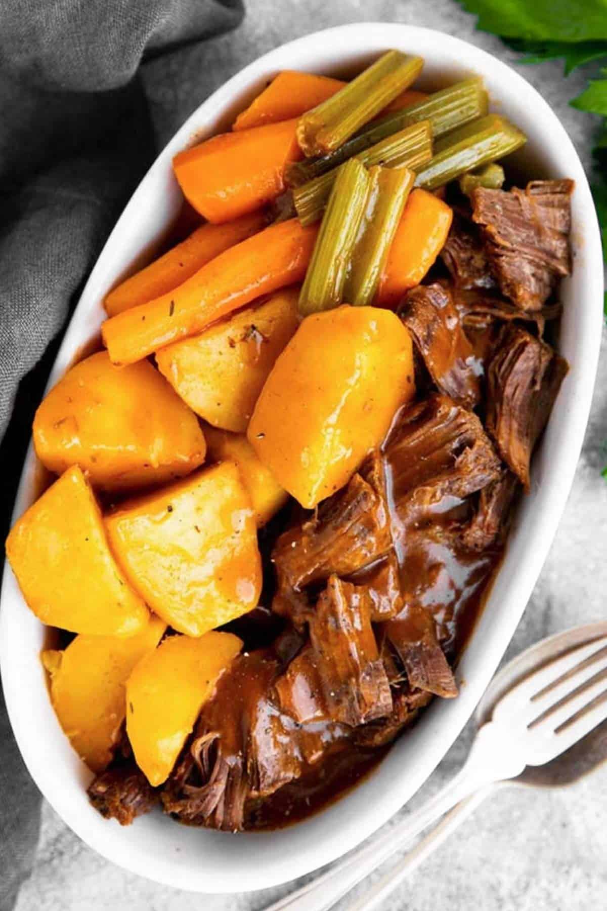 white dish with potatoes, carrots and beef roast in gravy