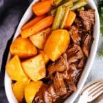 white dish with potatoes, carrots and beef roast in gravy