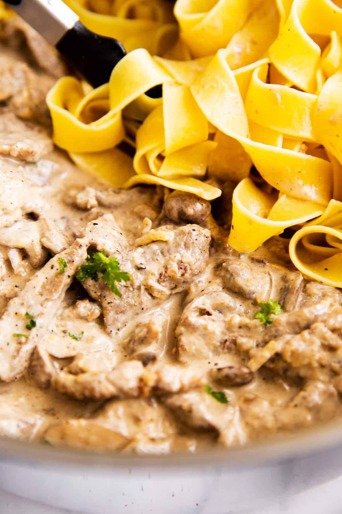 close up photo of beef stroganoff with noodles in the background