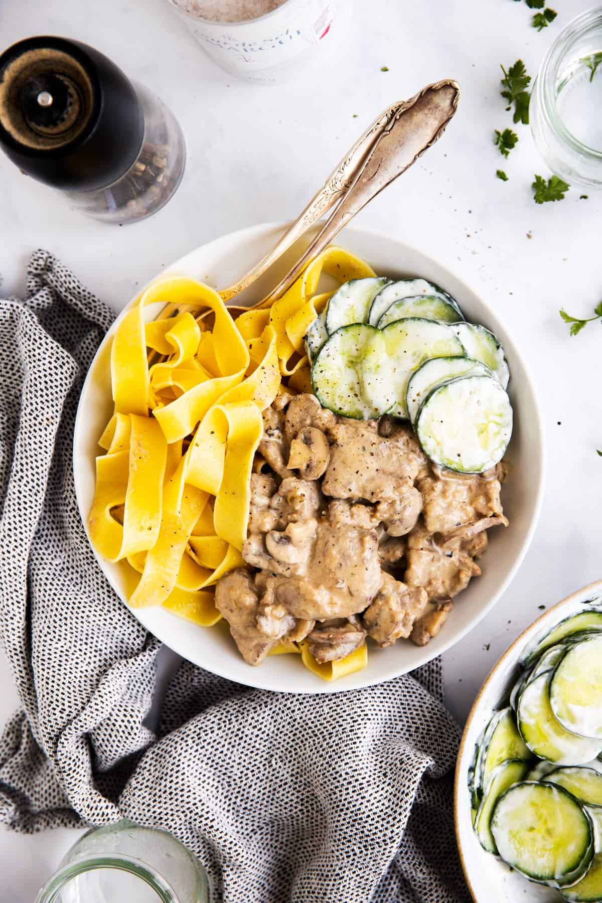 view from overhead on a white plate with stroganoff, egg noodles and cucumber salad