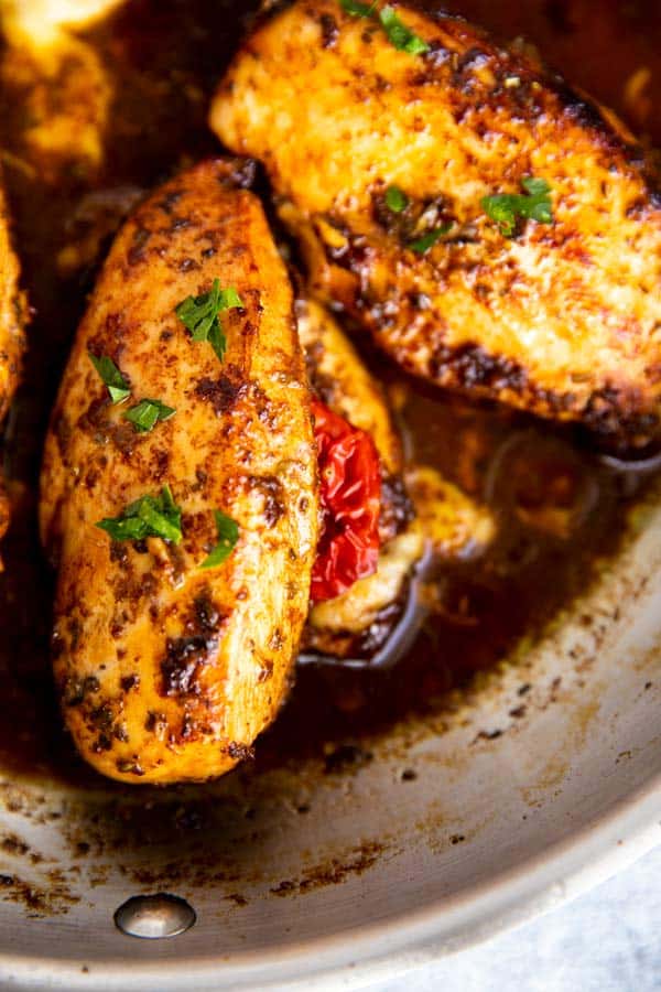 two chicken breasts with caprese filling in a pan with balsamic glaze