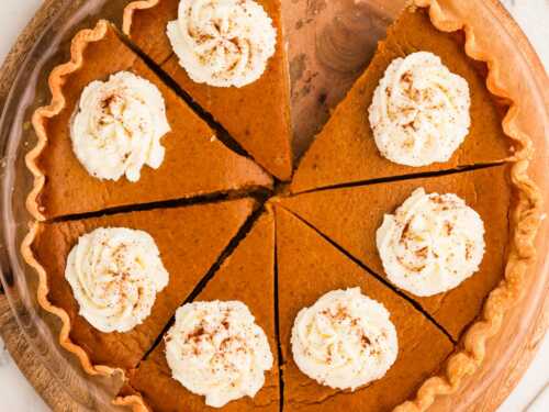 overhead view of sliced pumpkin pie decorated with whipped cream