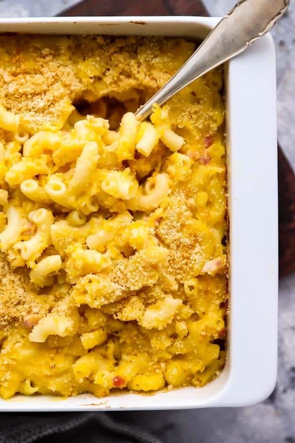 a white baking dish filled with butternut squash mac and cheese, with a serving spoon