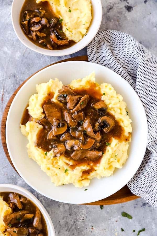 three plates with crockpot beef tips and gravy over mashed potatoes