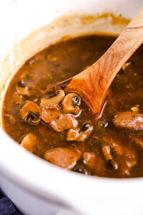 slow cooker with beef tips and mushroom gravy, with a wooden spoon in it