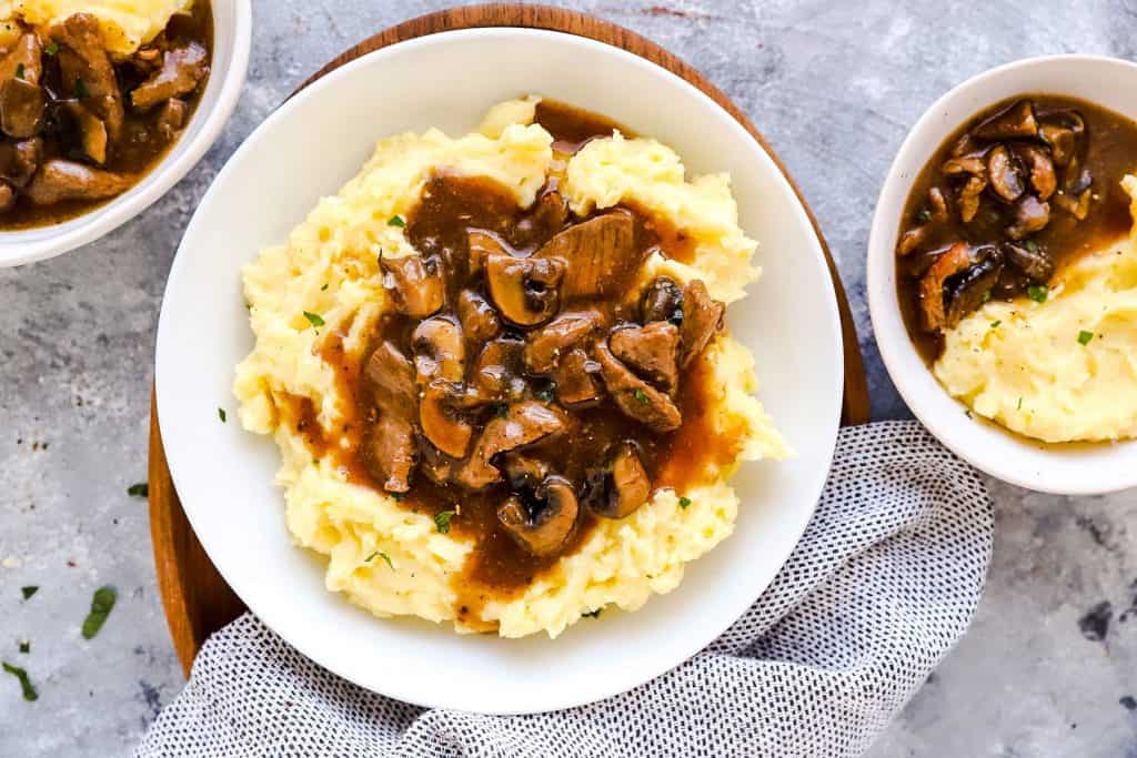 three plates with mashed potatoes and beef tips on a light surface