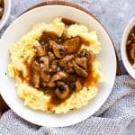 three plates with mashed potatoes and beef tips on a light surface