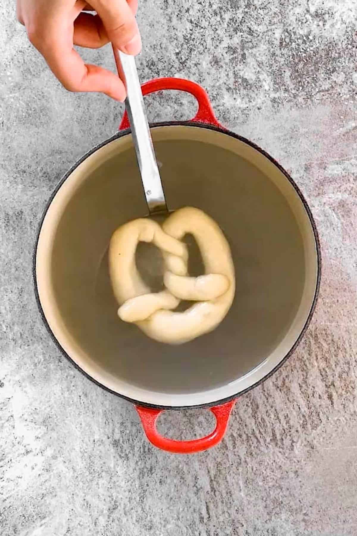 dipping unbaked pretzel in a pot of brine