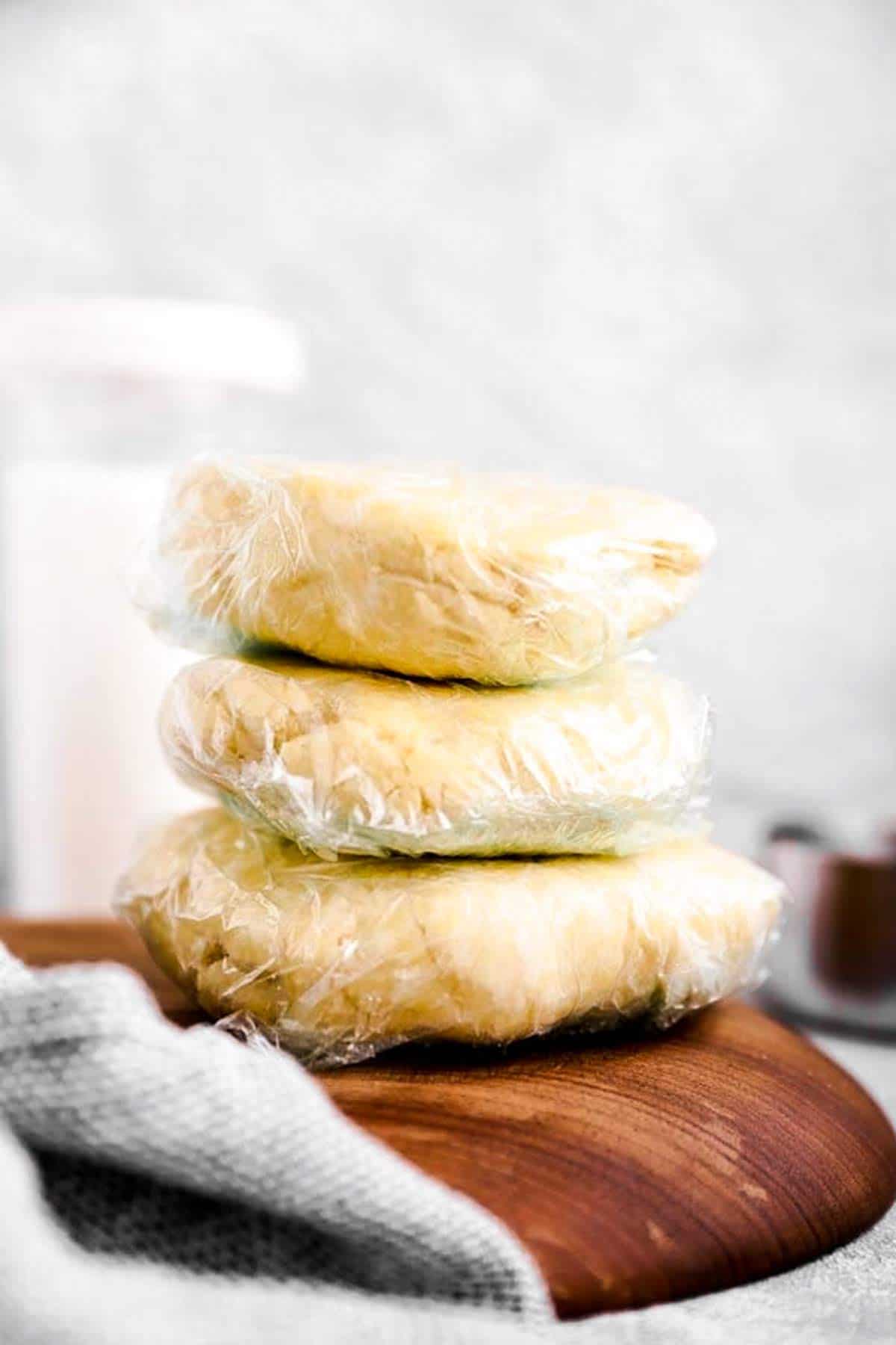 stack of wrapped pie crust discs on wooden board