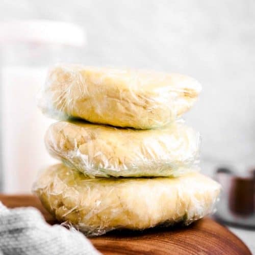 stack of wrapped pie crust discs on wooden board