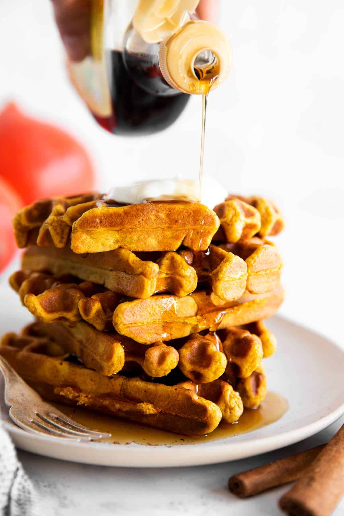 drizzling maple syrup over stack of pumpkin waffles