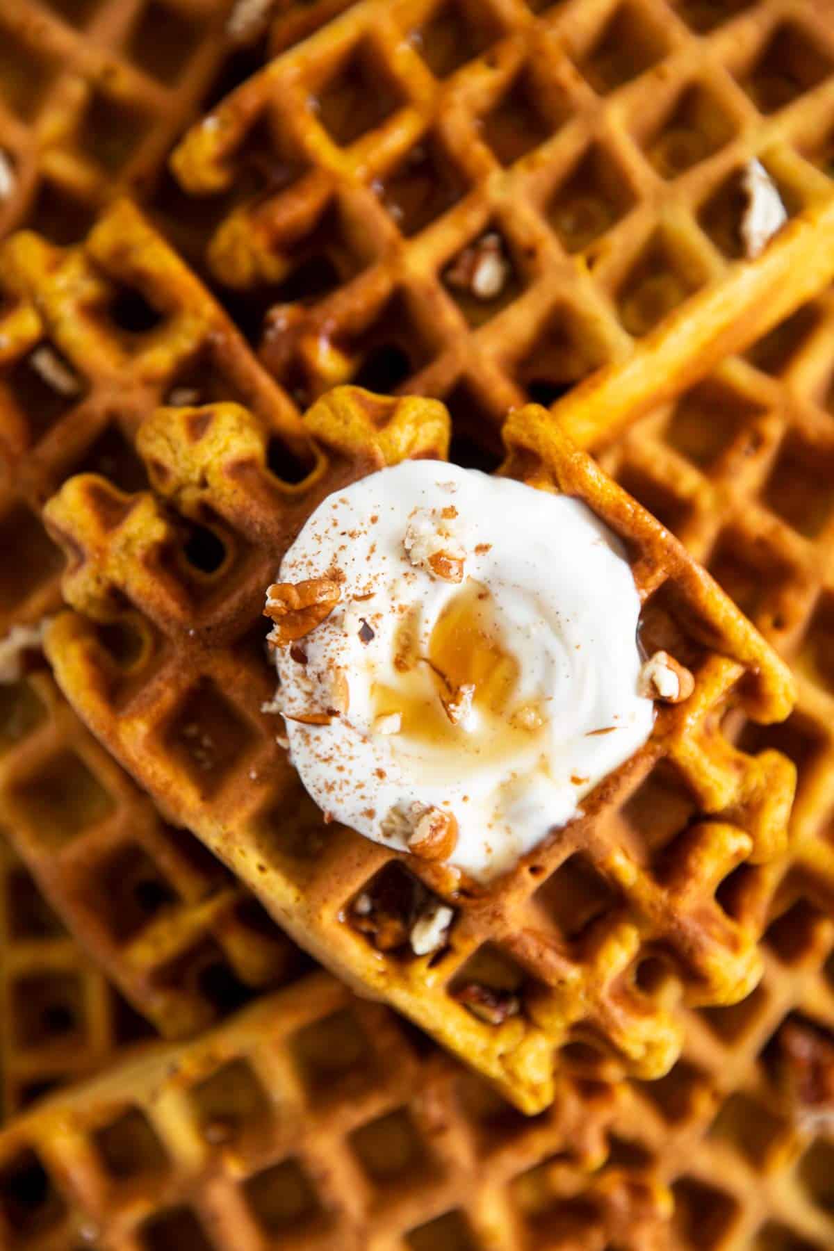 close up of pumpkin waffles with frosting and maple syrup