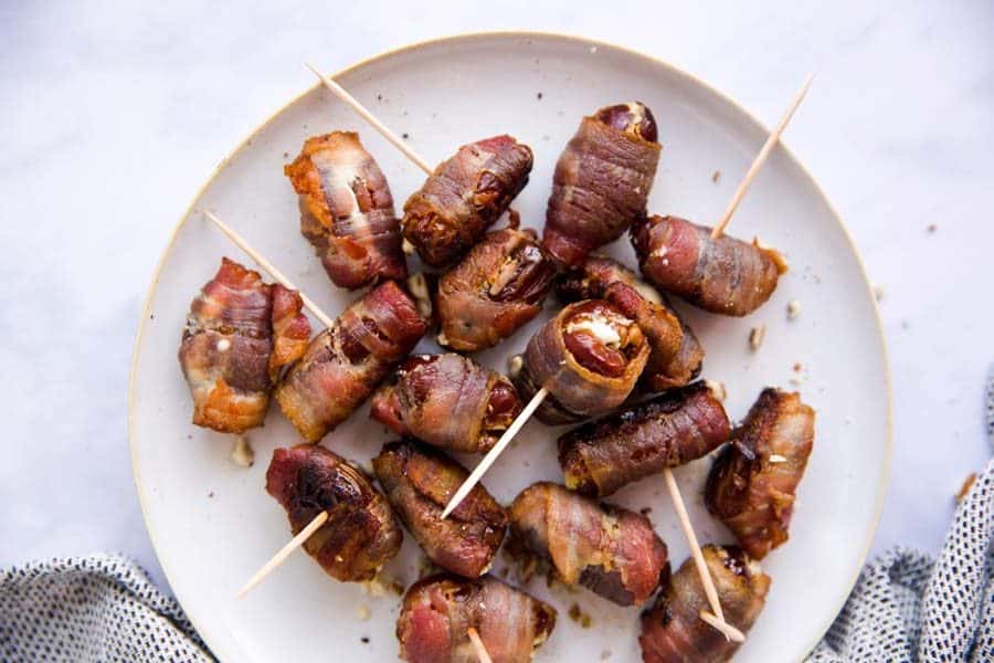 top down view on white plate filled with bacon wrapped dates