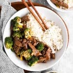 overhead view of beef and broccoli in white bowl with chopsticks