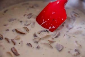 skillet with cream sauce, chicken and mushrooms, red spatula stirring