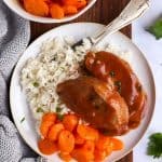 plate with rice, carrots and glazed pork chops on a wooden board