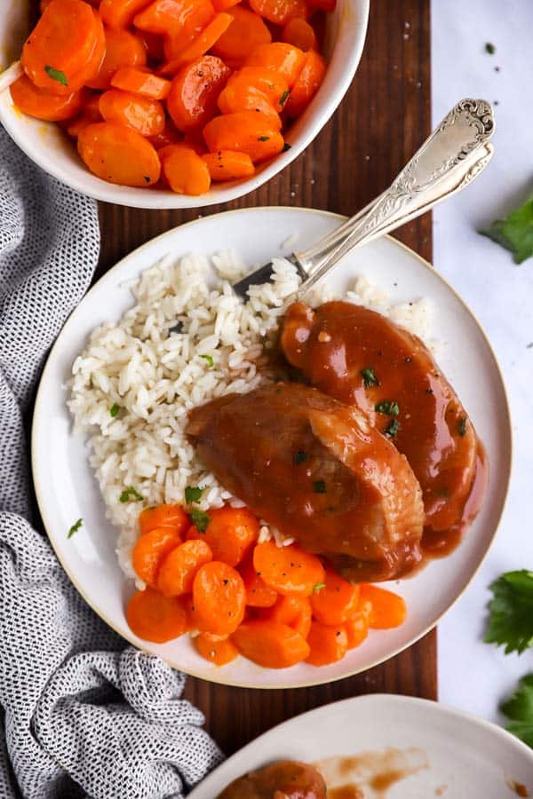 plate with rice, carrots and glazed pork chops on a wooden board