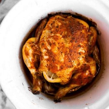 Whole seasoned chicken in a white crock of a slow cooker
