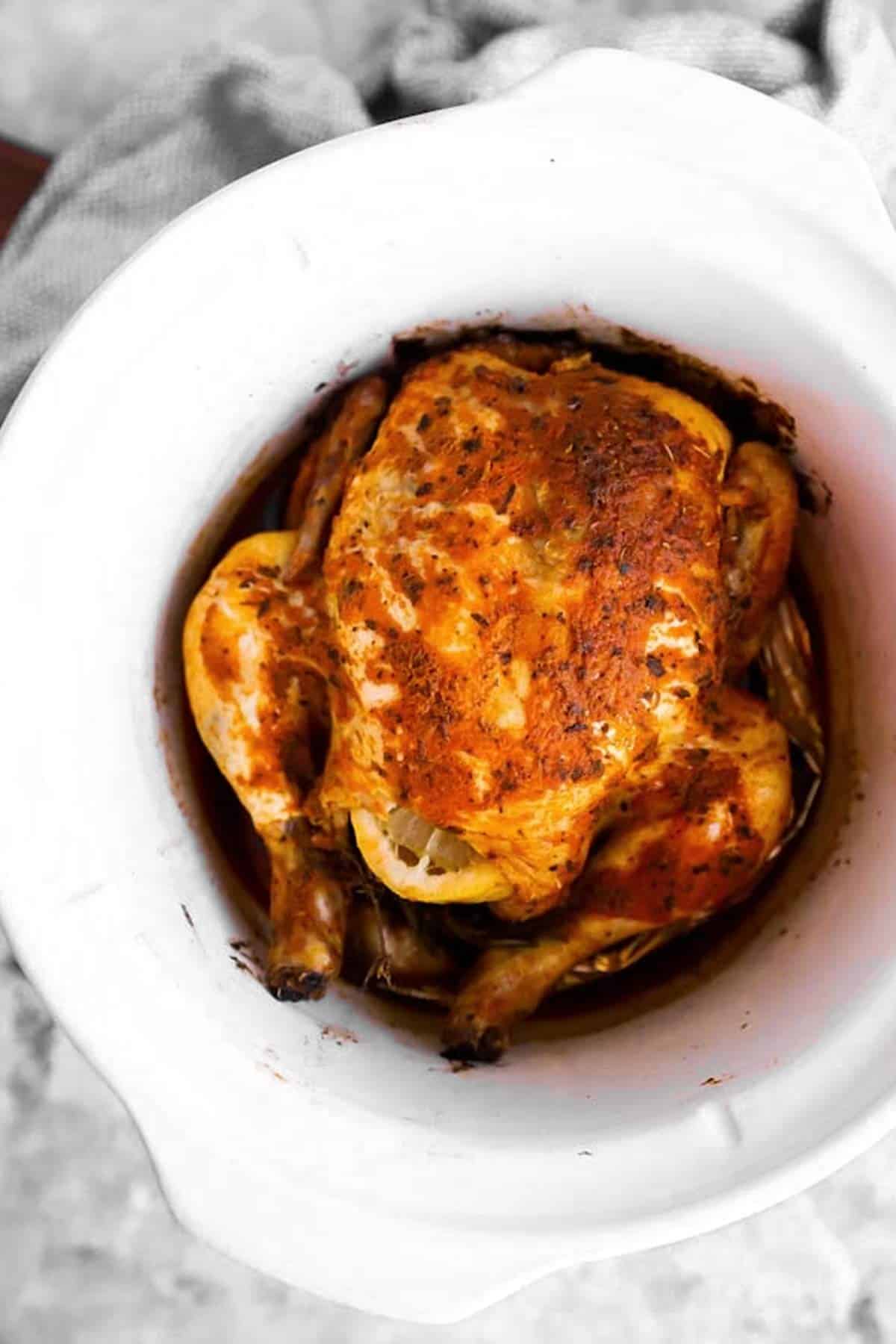 Whole seasoned chicken in a white crock of a slow cooker