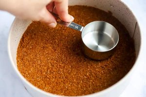 using a measuring cup to press a crust into a round pan