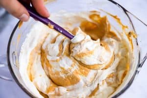 folding pumpkin filling and whipped cream together using a purple spatula