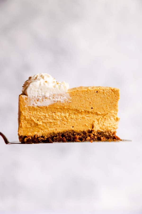 slice of no bake pumpkin cheesecake in front of a light colored wall