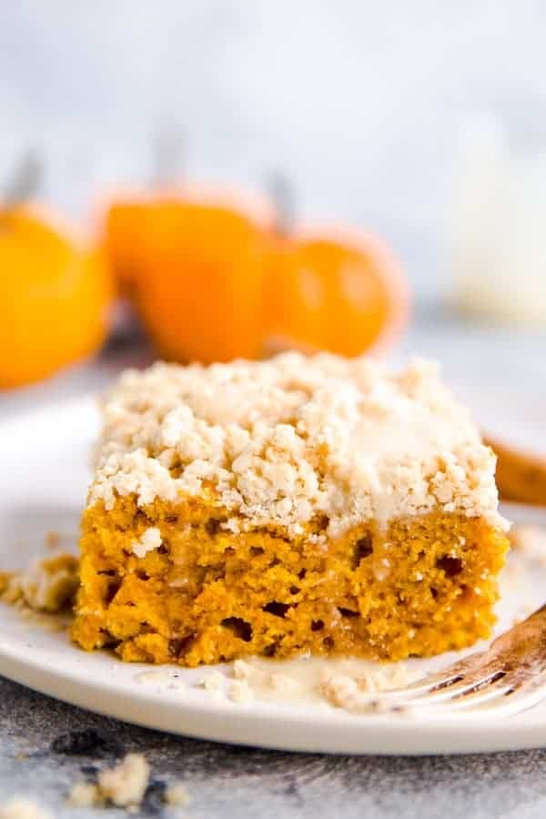 slice of streusel pumpkin coffee cake on a white plate with a few baby pumpkins in the background