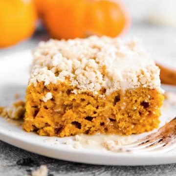 slice of streusel pumpkin coffee cake on a white plate with a few baby pumpkins in the background
