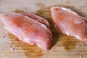 two chicken breasts on a chopping board with seasoning