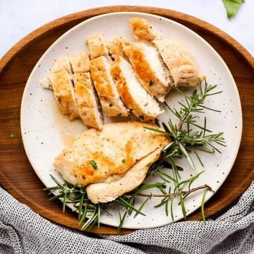 sliced chicken breast on a white plate, sitting on a wooden platter