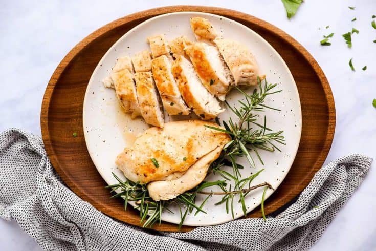 sliced chicken breast on a white plate, sitting on a wooden platter