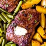 close up photo of a top sirloin steak with butter on a bed of green beans and roasted potatoes