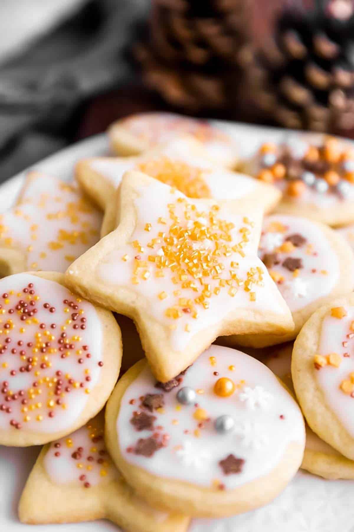 pile of cut out sugar cookies on plate in front of winter greenery