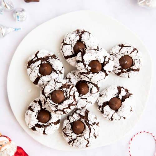 white plate with chocolate crinkle blossom cookies on a marble surface surrounded by festive elements