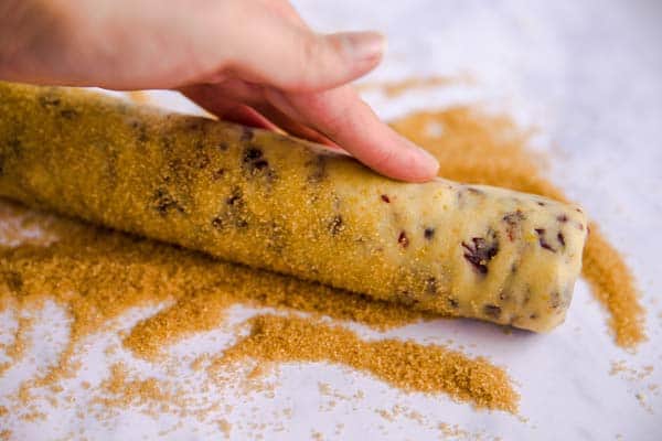 rolling a log of cookie dough in brown sugar