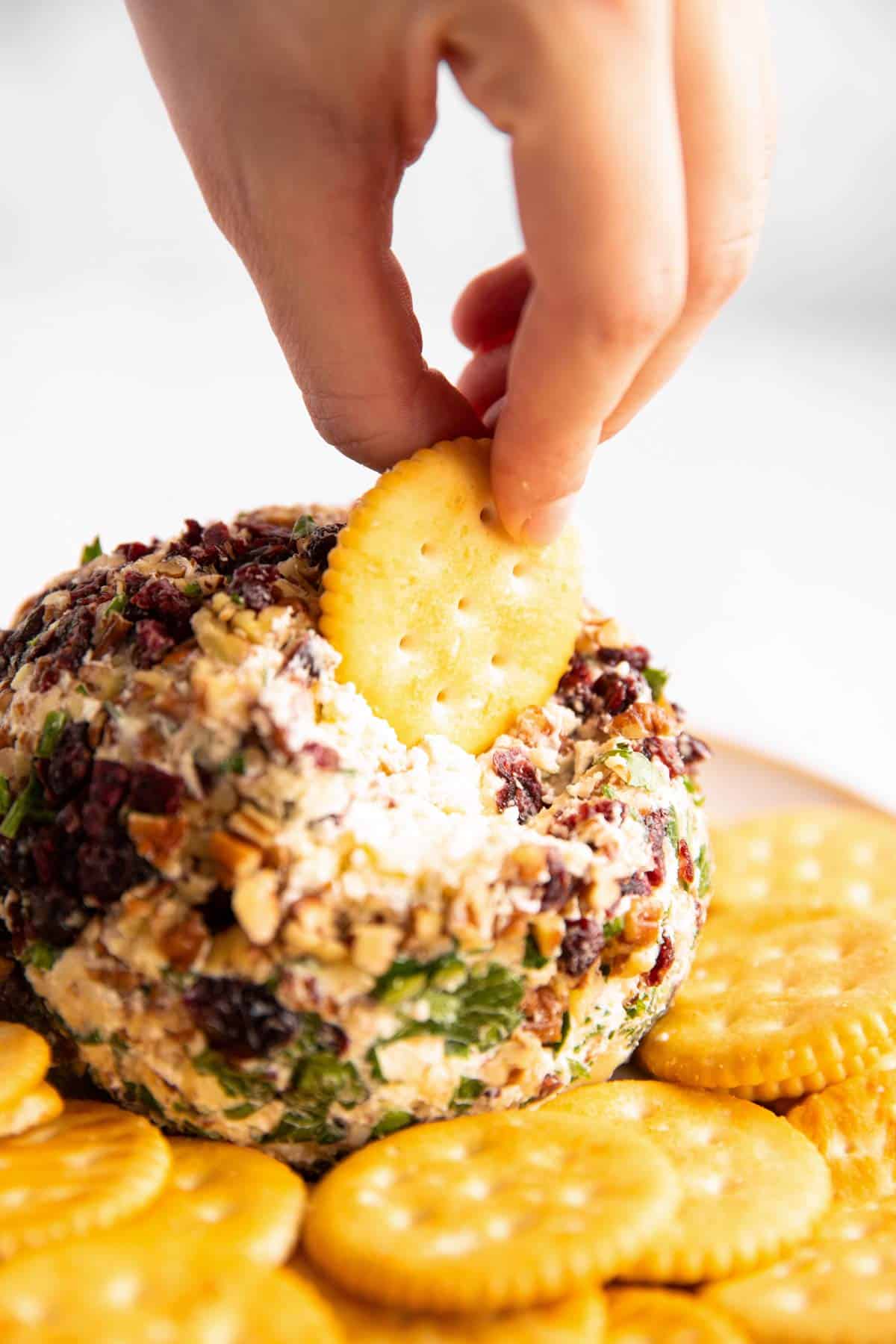 female hand dipping cracker into cheeseball