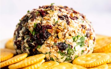 cheeseball rolled in chopped pecans, dried cranberries and parsley sitting on a bed of Ritz crackers