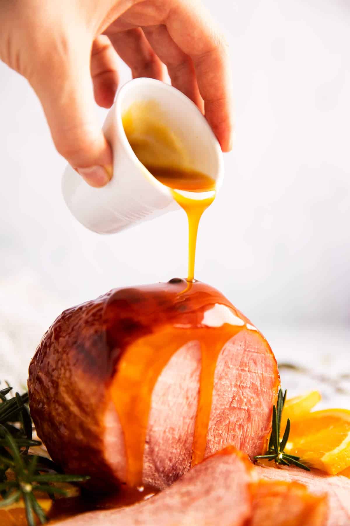 female hand drizzling honey glaze over ham