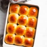 female hands holding a white pan filled with dinner rolls