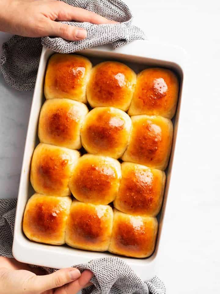 female hands holding a white pan filled with dinner rolls