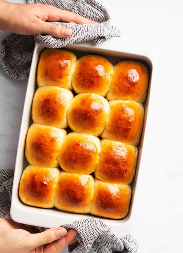 female hands holding a white pan filled with dinner rolls