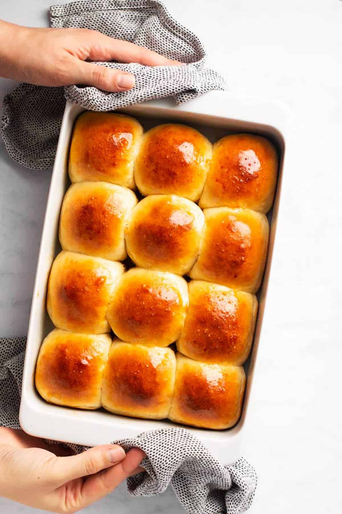 female hands holding a white pan filled with dinner rolls